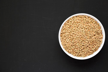 Organic green lentils in a white bowl on a black surface, overhead view. Flat lay, top view, from above. Space for text.