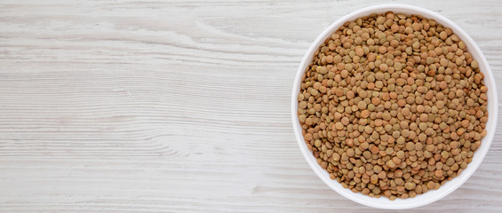 Organic green lentils in a white bowl on a white wooden table, top view. Flat lay, overhead, from above. Space for text.