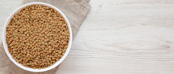 Organic green lentils in a white bowl on a white wooden surface, top view. Flat lay, overhead, from above. Copy space.