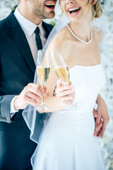 cropped view of bride and bridegroom clinking with champagne glasses
