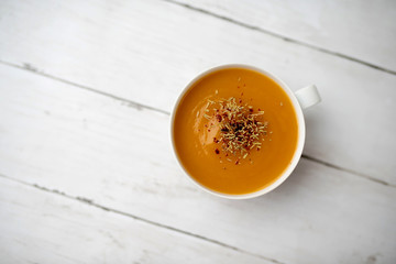 Creamy pumpkin squash vegetable soup in a white cup on white wood background