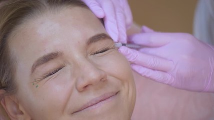 The doctor beautician makes injections in the face of the female patient. concept of beauty and cosmetology. 4k. biorevitalization The patient squints and smiles.