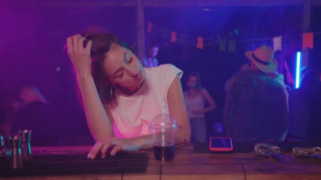 Beautiful lonely girl sitting alone at bar counter in the nightclub. Portrait of upset single girl getting bored at the party.