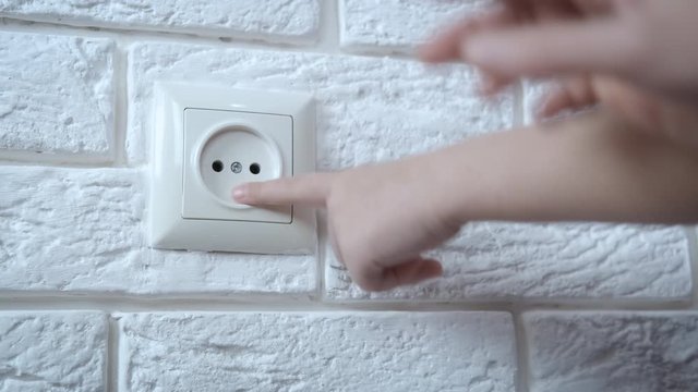A child touches an electrical outlet. The child's hands sticks his fingers into the socket.