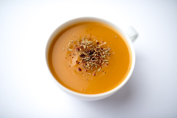 Creamy pumpkin squash vegetable soup in a white cup on white background