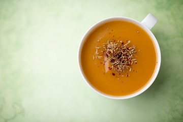 Creamy pumpkin squash vegetable soup in a white cup on green background