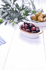 Traditional appetizers, green and red olives from Greek cuisine. White wood background. Fresh branches of olives. Copy space.