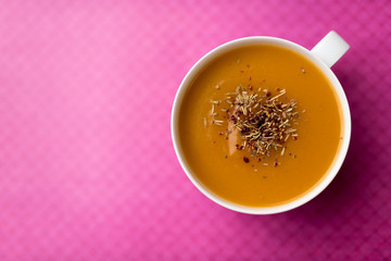 Creamy pumpkin squash vegetable soup in a white cup on pink background