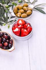 Traditional appetizers, olives from Greek cuisine. White wood background. View from above. Fresh branches of olives. Copy space.