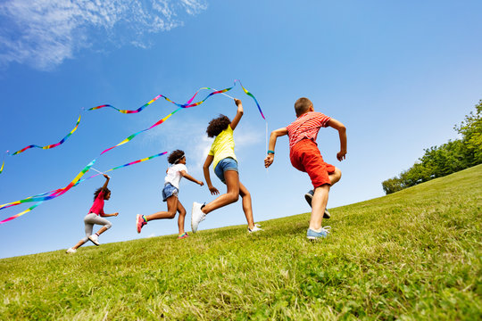 Children run colorful ribbons in park together