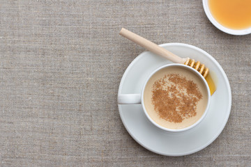 Spicy warming tea with milk in white porcelain cup with honey and honey dipper on textile...