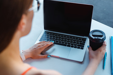 selective focus of girl typing on laptop with blank screen and holding coffee to go on table