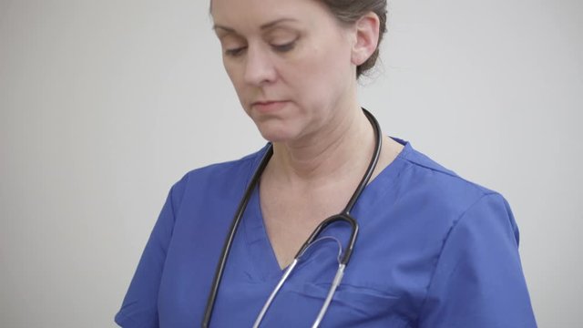 Close, tilting shot of a nurse reading and typing on a tablet in exam room