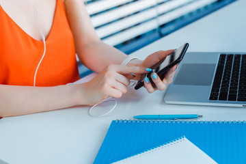partial view of woman using smartphone near laptop and stationery on table
