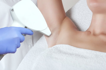 Naklejka premium The cosmetologist does the laser hair removal procedure in the armpit zone, to a young woman in a beauty salon.