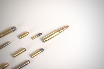 A large bullet (7.62 x 51mm NATO) leading a group of smaller bullets over a white surface.