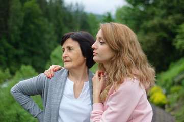 Fototapeta premium Outdoors portrait of happy senior woman and girl who are traveling together over landscape of forest and mountains. Concept of tenderness, care, family love, relationships.