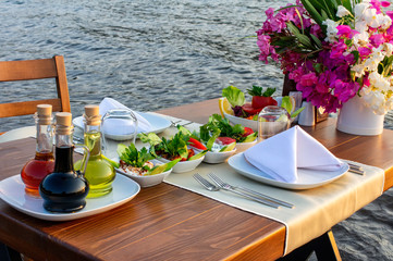 A romantic dinner table with healthy delicatessen on it, is placed in the sea at sunset