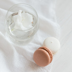 Two pastel French macarons  and glass with flower on a white background.