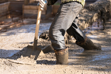 Raking concrete. Concrete for parking lot construction. A worker in boots flattens the concrete with a shovel.