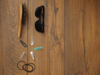 Woman's wooden brush, elastic bands, Black sunglasses and metal clips for hair on a wooden table surface, Copy space, Top view.