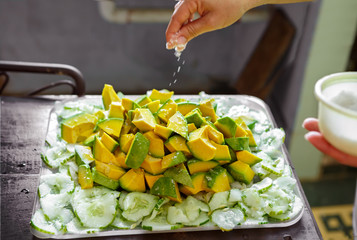 Tray of Avocado and Cucumber with Salt Being Sprinkled in a Cuban Kitchen