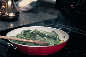 Breakfast in the village. Cooking spinach with scrambled eggs in red pan.