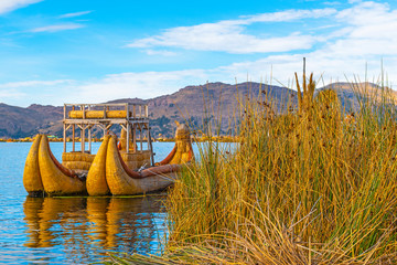 A totora reed boat by the Uros floating islands at sunrise with the Andes mountain range in the background near Puno, Peru, South America.