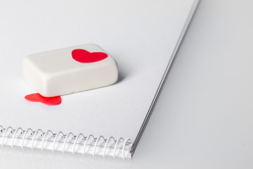 a white eraser and two red paper hearts on a white booklet