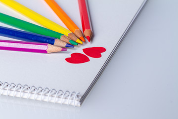 rainbow of coloring pencils around two red paper hearts on a booklet