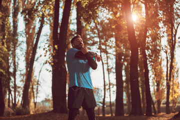 Young man stretching bodies, warming up for jogging in public park.