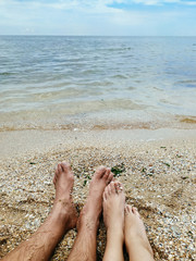 Male and female feet in the sand from a shell rock. Couple relaxing on a tropical beach. The concept of relaxation, honeymoon, sunbathing on the beach.