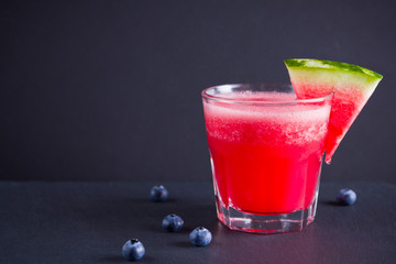 Watermelon drink in glasses with slices of watermelon. Watermelon smoothies and blueberries on dark background. Summer healthy drink for vegetarian. Copy space