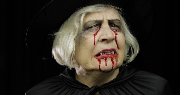 Old witch Halloween makeup. Elderly woman portrait with blood on her face.