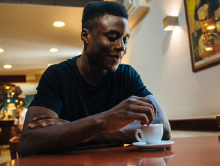Young black man drinking coffee sitting in cafeteria.