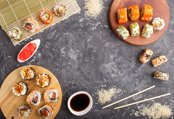 Different kinds of Japanese maki sushi rolls with salmon, sesame, cheese, roe and chopsticks, soy sauce, marinated ginger on a black concrete background. Top view.