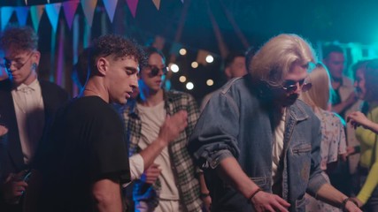 Jolly party time. Handsome stylish young people dancing into music at night party. Focus on cool blondie boy performing cool dance.