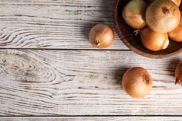 Bowl and ripe onions on white wooden table, flat lay. Space for text
