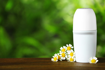 Natural roll-on deodorant with chamomile flowers on wooden table against blurred green background. Space for text