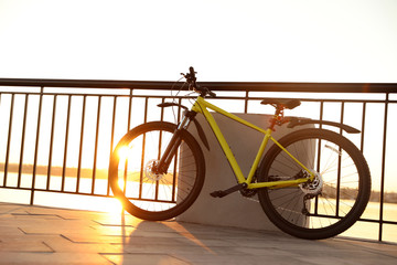 Yellow bicycle parked near railing on city waterfront at sunset