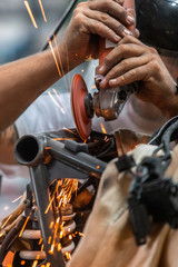 Worker cutting, grinding and polishing motorcycle metal part with sparks indoor workshop, close-up
