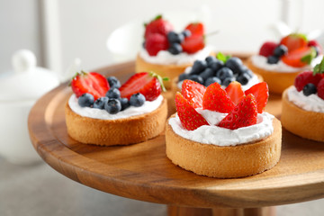 Cake stand with different berry tarts on table. Delicious pastries - obrazy, fototapety, plakaty