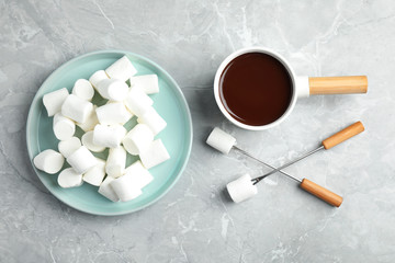 Fondue pot with dark chocolate and marshmallows on marble table, flat lay