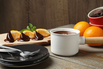 Fondue pot with milk chocolate and oranges on wooden table