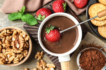 Dipping strawberry into fondue pot with milk chocolate on wooden table, top view