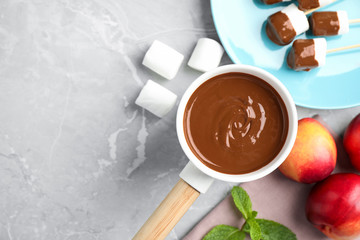 Fondue pot and marshmallow dipped into milk chocolate on light table, flat lay. Space for text