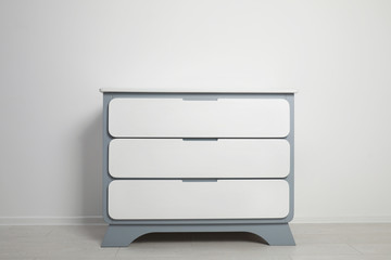 Modern wooden chest of drawers at light wall