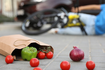 Woman fallen from bicycle after car accident outdoors, focus on scattered vegetables