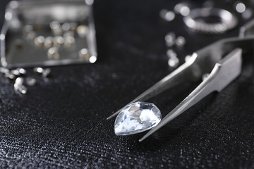 Jewel and tweezers on black leather surface