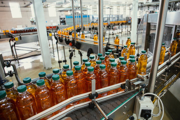 Conveyor line with plastic bottles of juice at modern factory equipment. Beverage manufacturing plant interior inside